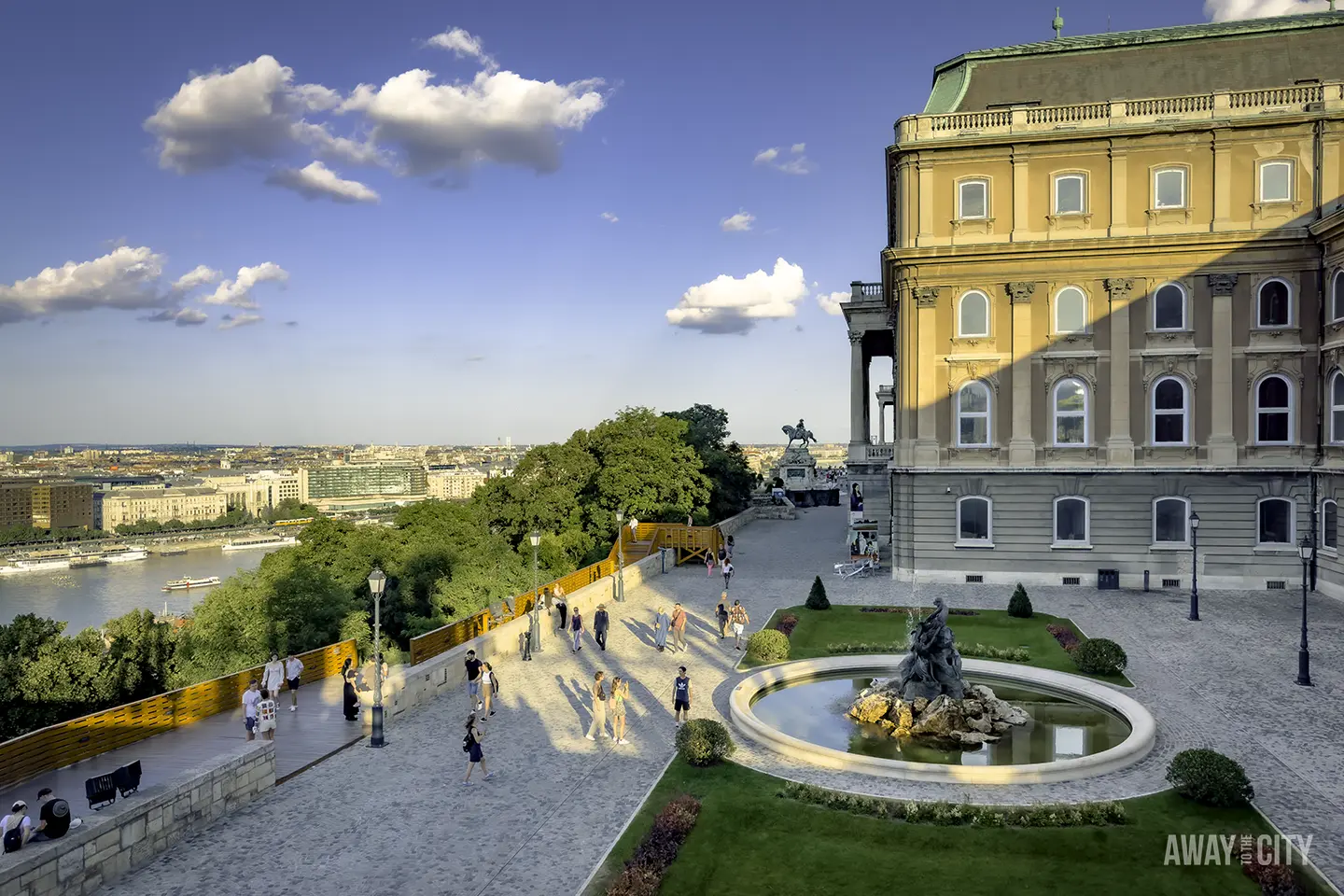 A group of people walking on a path with a fountain in front of Buda Castle, housing the Hungarian National Gallery in Budapest.