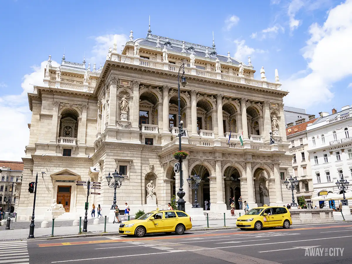 The exterior of the Budapest Hungarian State Opera House with two yellow taxis parked in front of it.