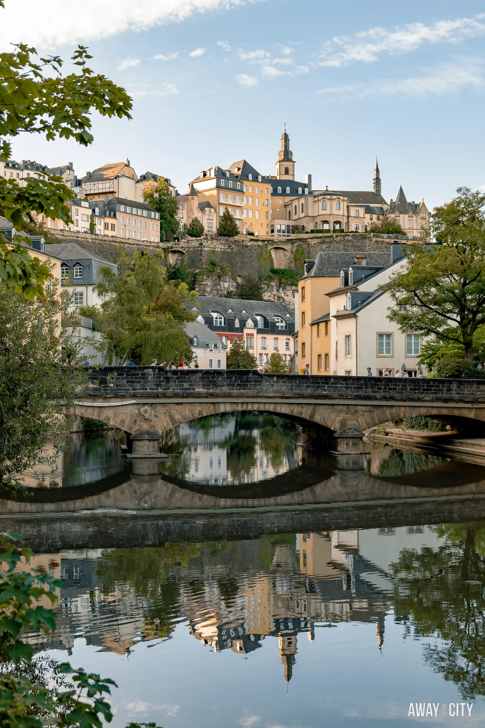 A picture of the Pont du Grund, also known as Pont du Stierchen Bridge, spanning the Alzette River in Luxembourg City's Grund District, with buildings in the background