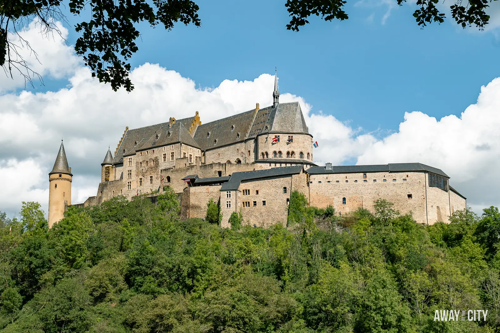 A panoramic view of Vianden Castle in Luxembourg perched on a hillside, overlooking the town of Vianden