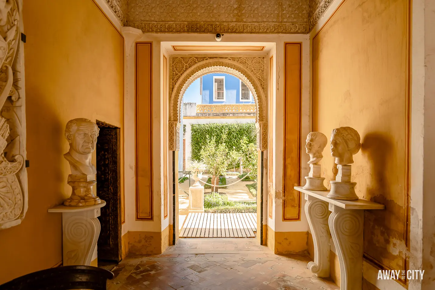 A doorway leading to one of the gardens of Casa de Pilatos in Seville, with statues on a table.