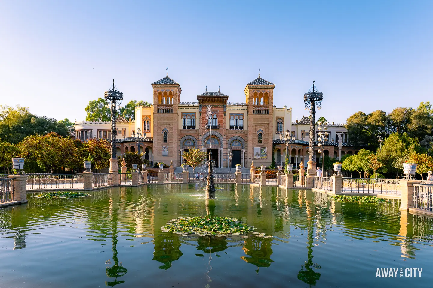 A picture of a Fountain and the Museum of Arts and Popular Customs in the background in Parque de María Luisa, Seville.