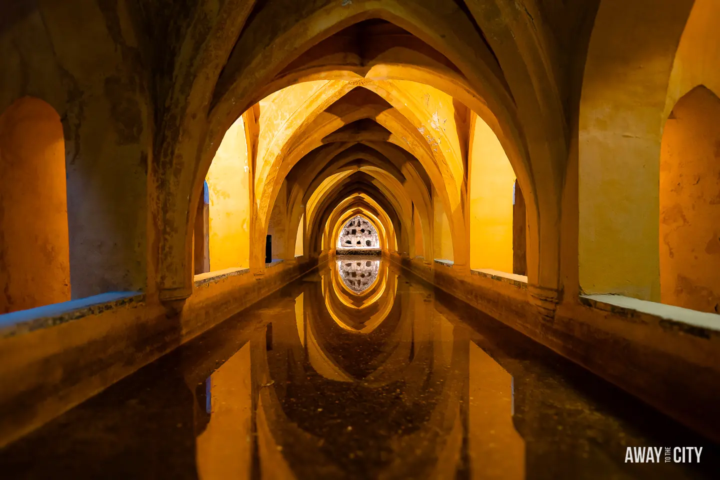 A picture of a long hallway with arches and water, depicting the underground baths of Maria de Padilla in Real Alcazar (also known as Royal Alcázar of Seville).