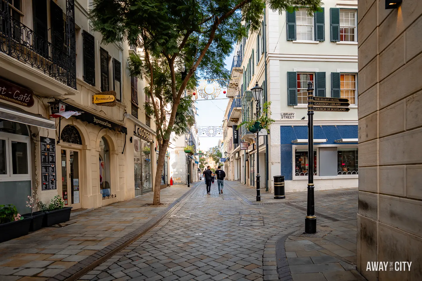 A picture of two people walking on a cobblestone street, showing Gibraltar's Main Street in Gibraltar.