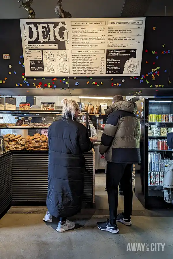 A couple of people standing in front of the American-style bakery Deig in Reykjavik, known for its pancakes, cinnamon rolls, and hearty sandwiches.
