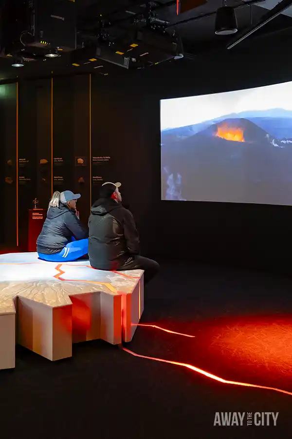 People sitting on a table in a room in the "Forces of Nature" exhibition with a large screen, where you can learn about the power of volcanoes, earthquakes, and geothermal energy in the Perlan museum in Reykjavik.