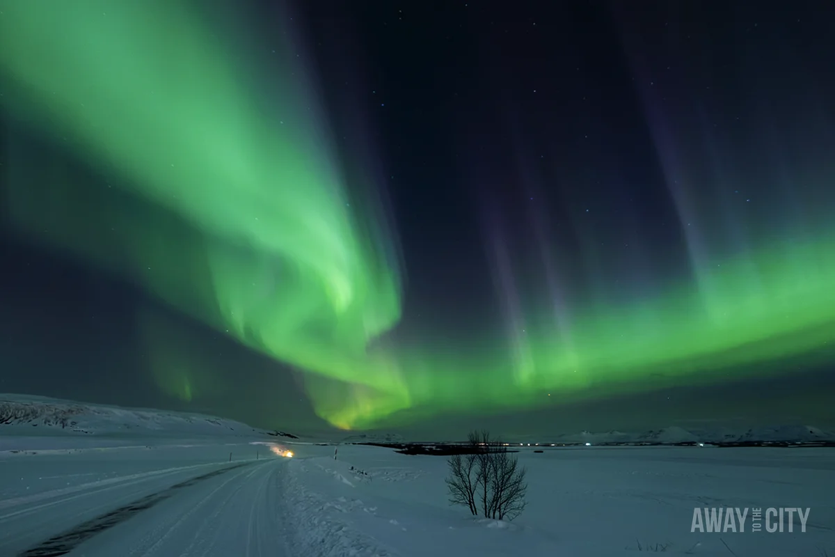 A snowy landscape under a dark night sky is illuminated by the green hues of the Aurora Borealis.