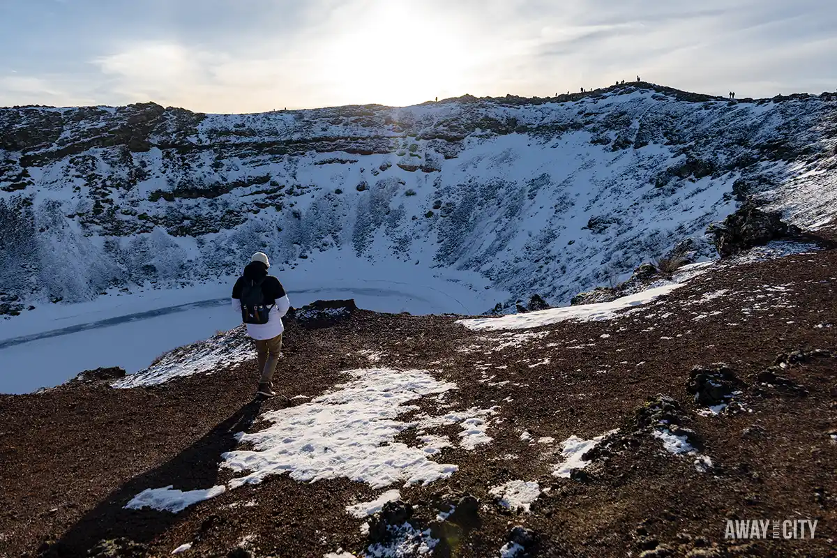 A person walking on the snow-covered rim of the Kerid Volcanic Crater on a Golden Circle day tour from Reykjavik, one of the best things to do in winter.