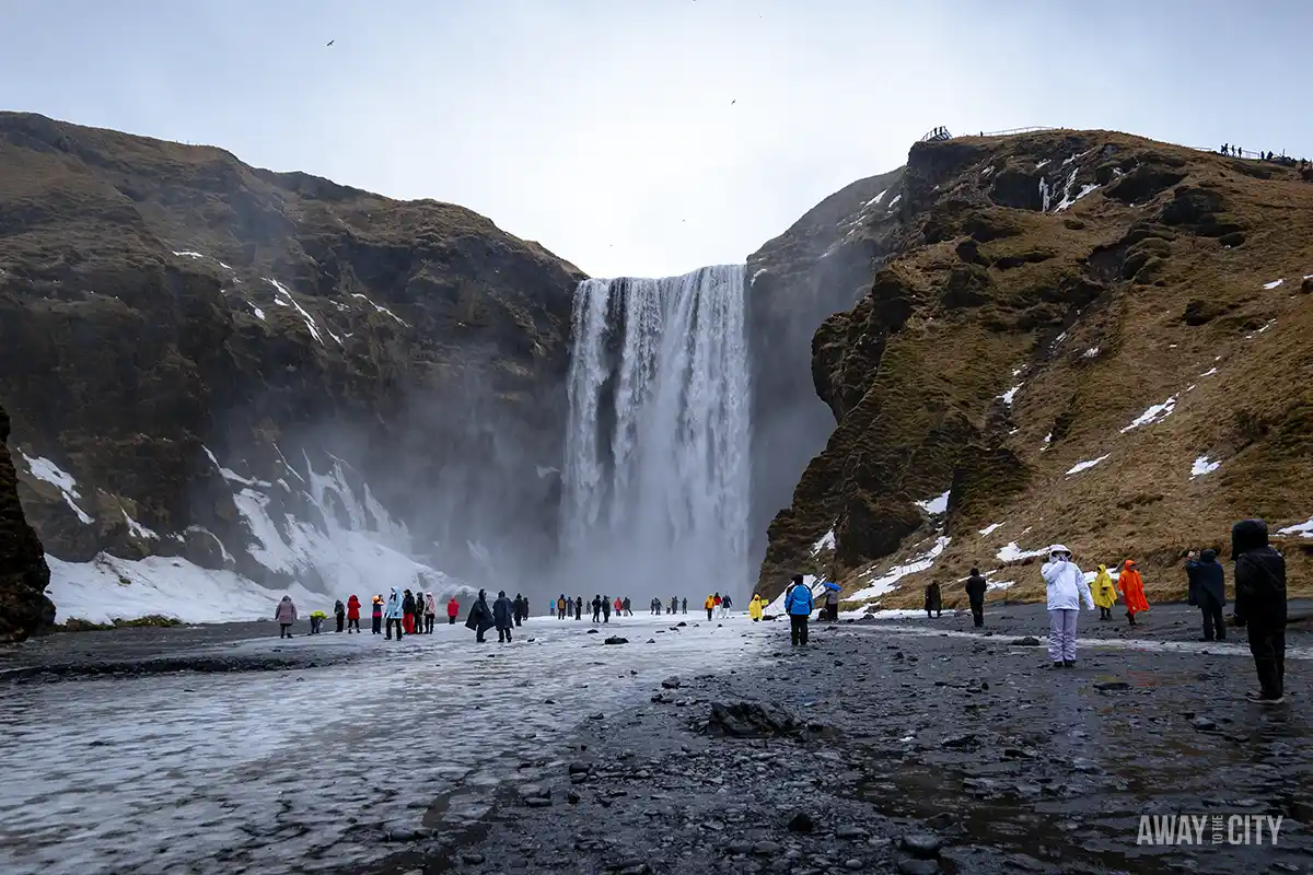 A group of people standing in front of Skógafoss, a powerful and picturesque waterfall along Iceland's South Coast, one of the best things to do from Reykjavik in winter.