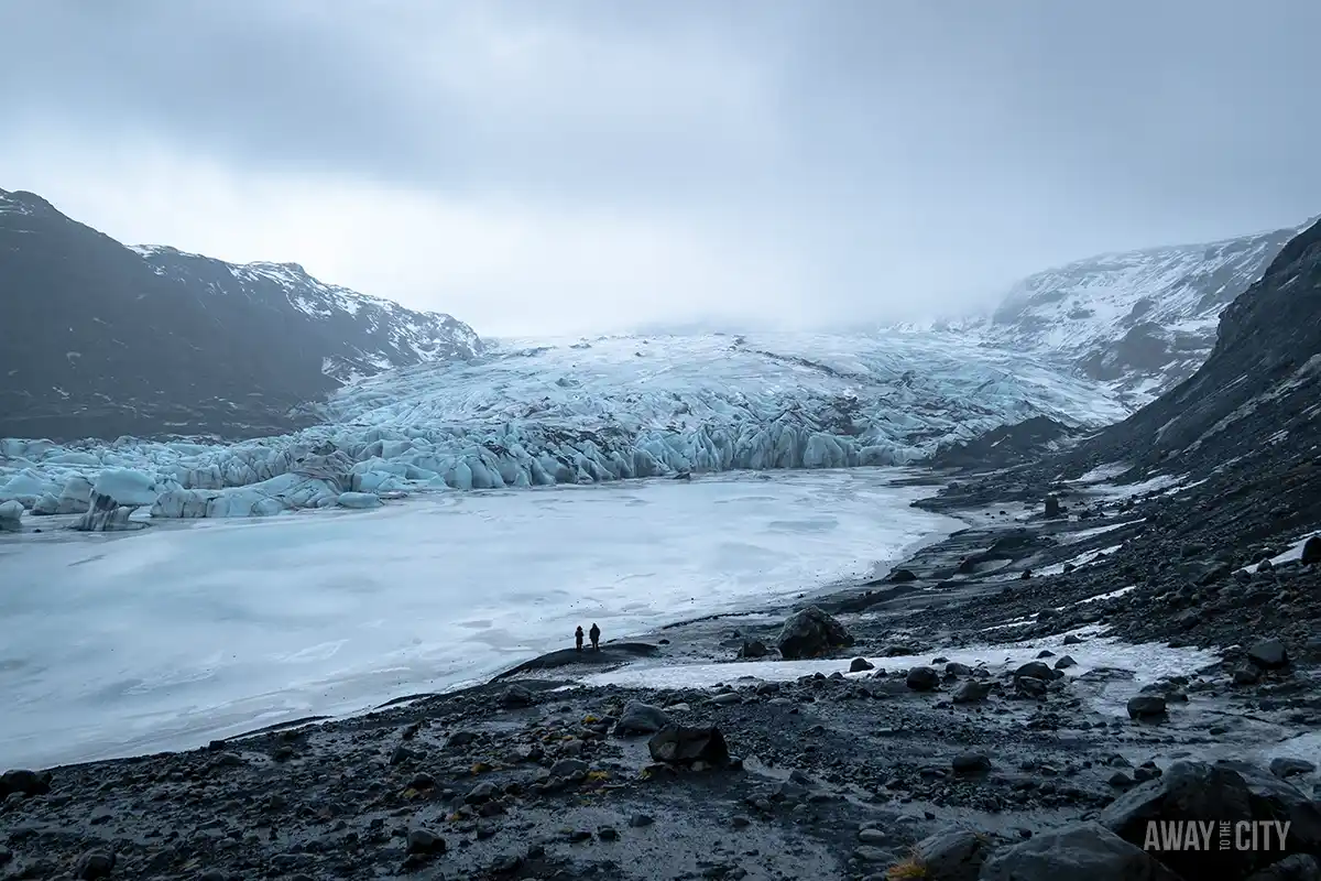 A rocky landscape with a lake and snowy mountains at the Sólheimajökull Glacier on a day tour to Iceland's South Coast, one of the best things to do from Reykjavik in winter.
