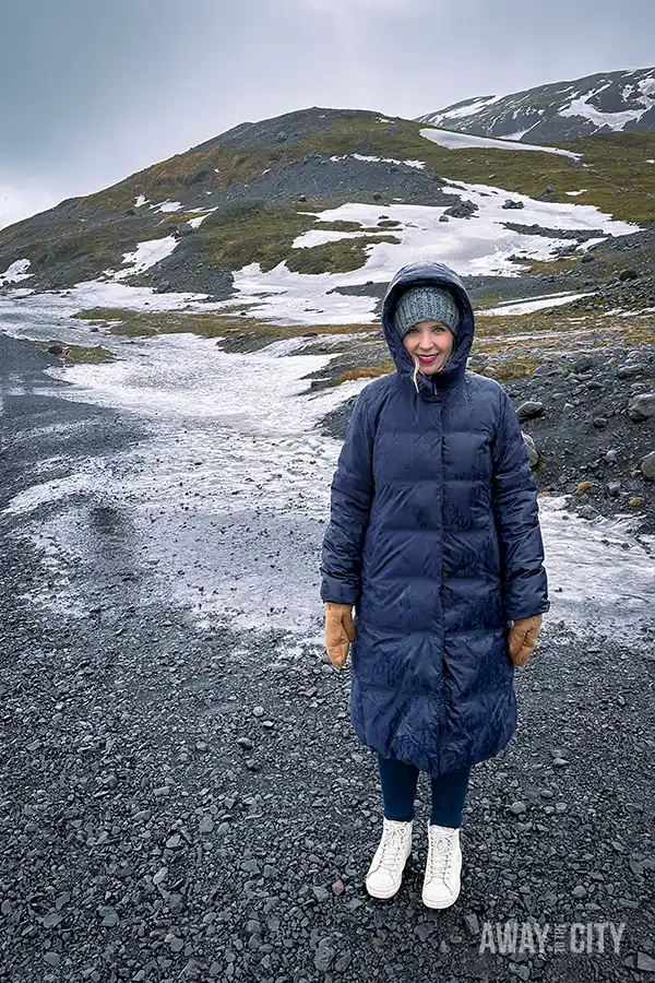 A person standing in a rocky area with snow covered mountains in the background, taken on a day tour to Iceland's South Coast, one of the best things to do from Reykjavik in winter.