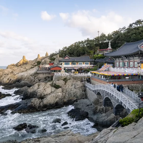 A bridge over a rocky beach and the Haedong Yonggungsa Temple in the background.