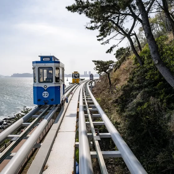 A blue and yellow retro-looking capsule on the track of the Busan Sky Capsule, with the sea in the background, taken at Haeundae Blueline Park in Busan, South Korea.