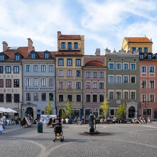 A group of people in a square with buildings in the background, taken at Warsaw's Old Town Market Place in Poland.