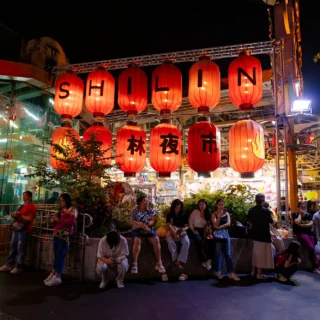 A group of people sitting outside a night market in Taipei with lanterns in front of it, saying Shilin.