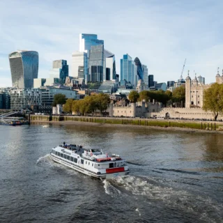 A boat on the water, with the City of London and the Tower of London in the background.