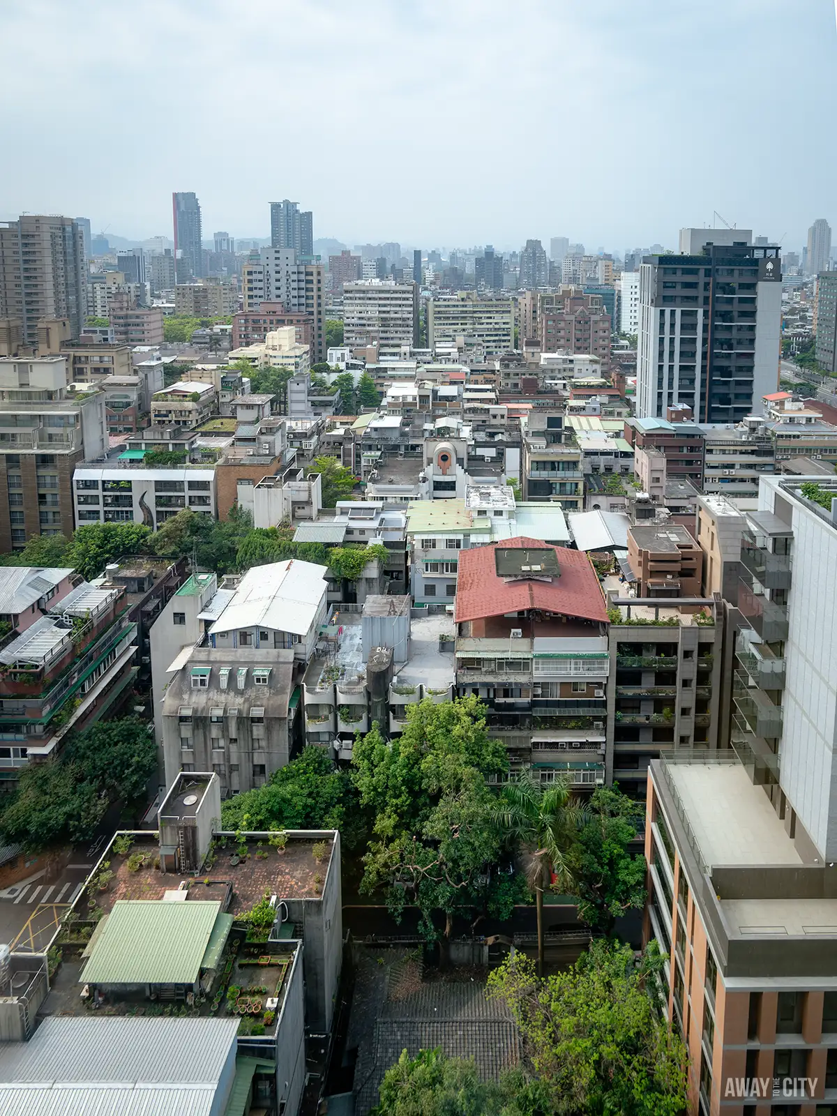 An aerial view of a densely populated urban area with various buildings and greenery, with the text "Away To The City" in the bottom right corner.