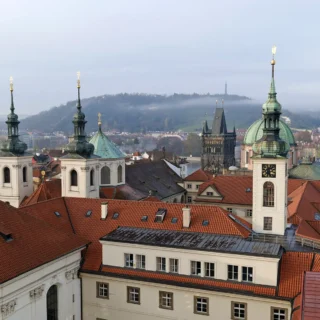 A panoramic view of Prague's skyline showcasing numerous church spires and rooftops with the iconic Charles Bridge visible in the distance.