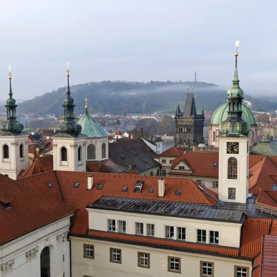 A panoramic view of Prague's skyline showcasing numerous church spires and rooftops with the iconic Charles Bridge visible in the distance.