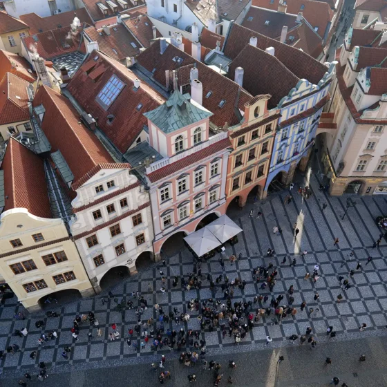 A bird's-eye view of the bustling Old Town Square in Prague, with colourful buildings, crowds of people, and the intricate paving of the square.