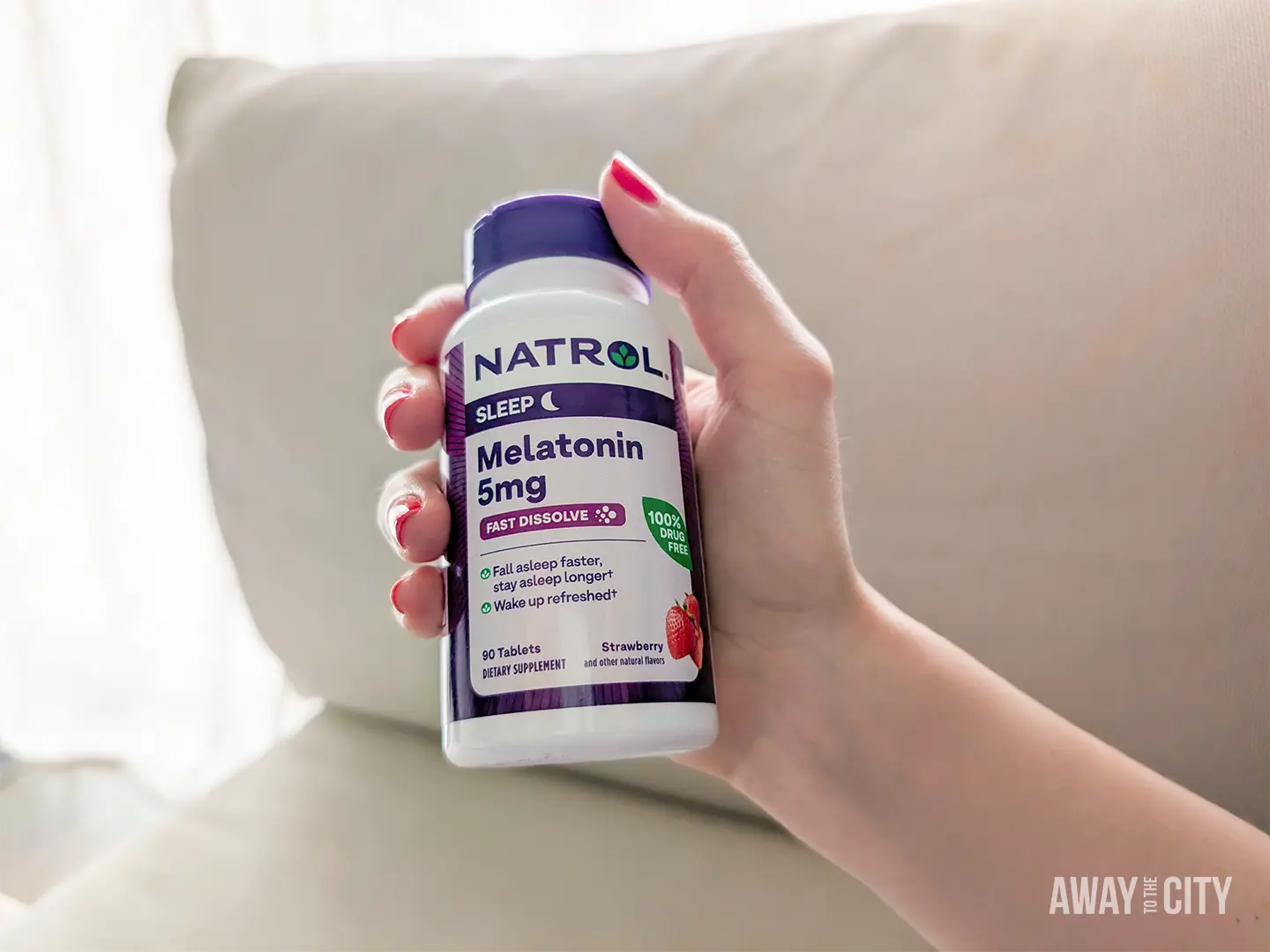 Hand holding a bottle of Natrol Melatonin 5mg tablets, used to help with falling asleep and managing jet lag.