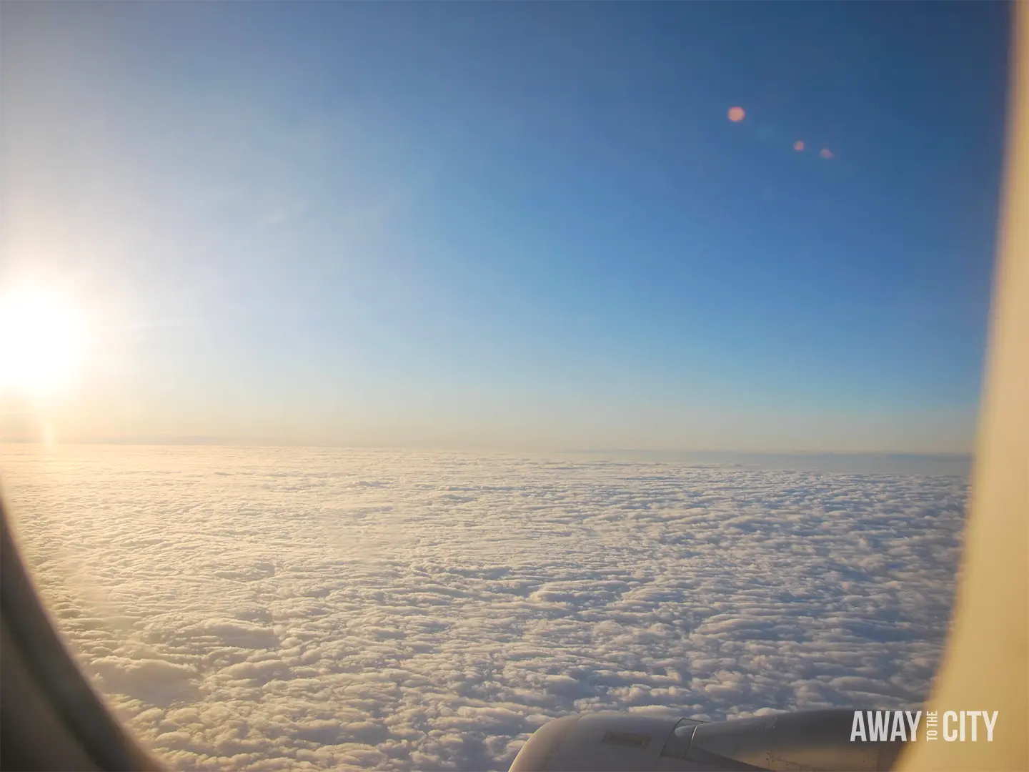 Sunset above a vast blanket of clouds, viewed through an aeroplane window during a flight.