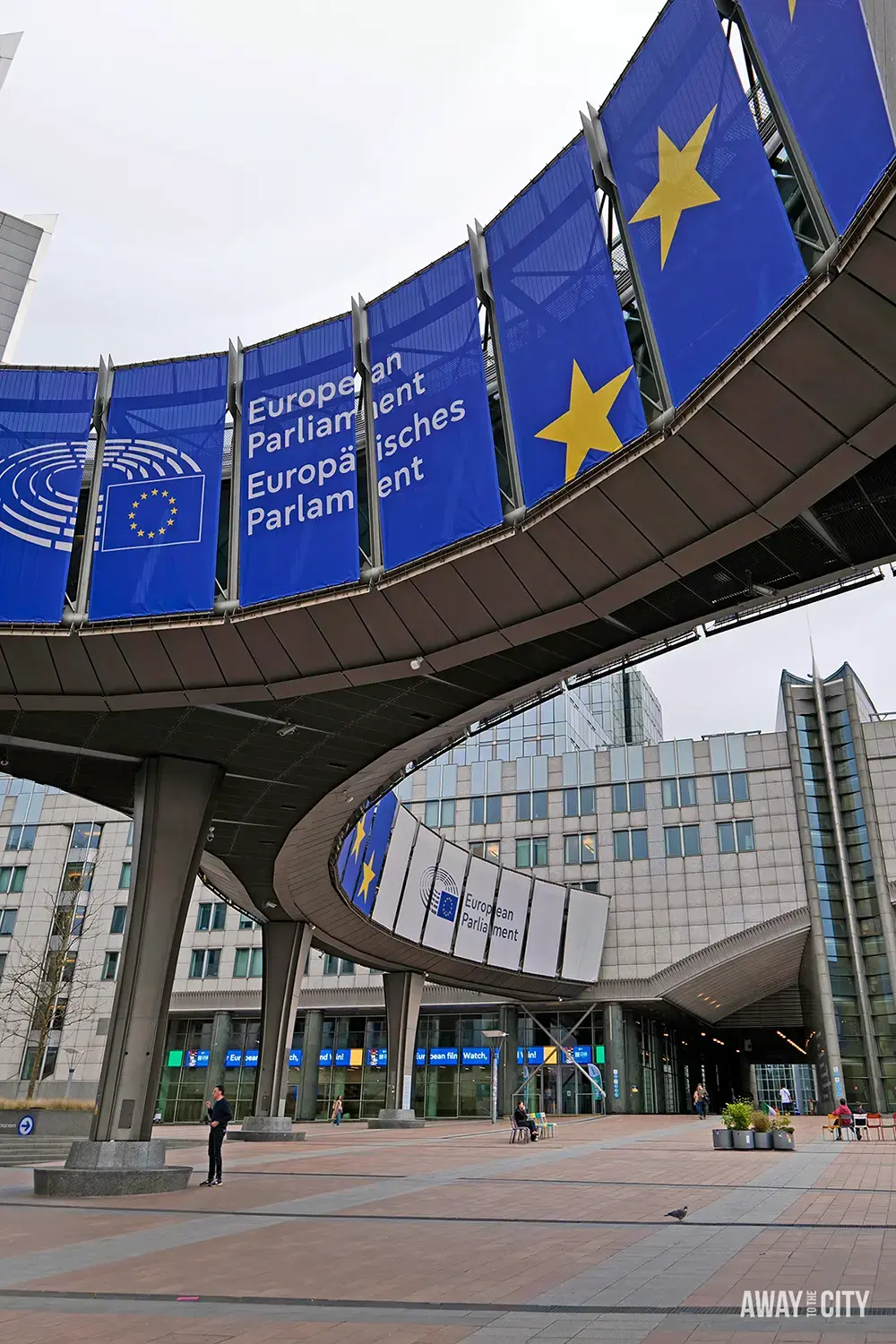 Curved entrance of the European Parliament building with large blue banners reading European Parliament and Europäisches Parlament, featuring yellow EU stars.
