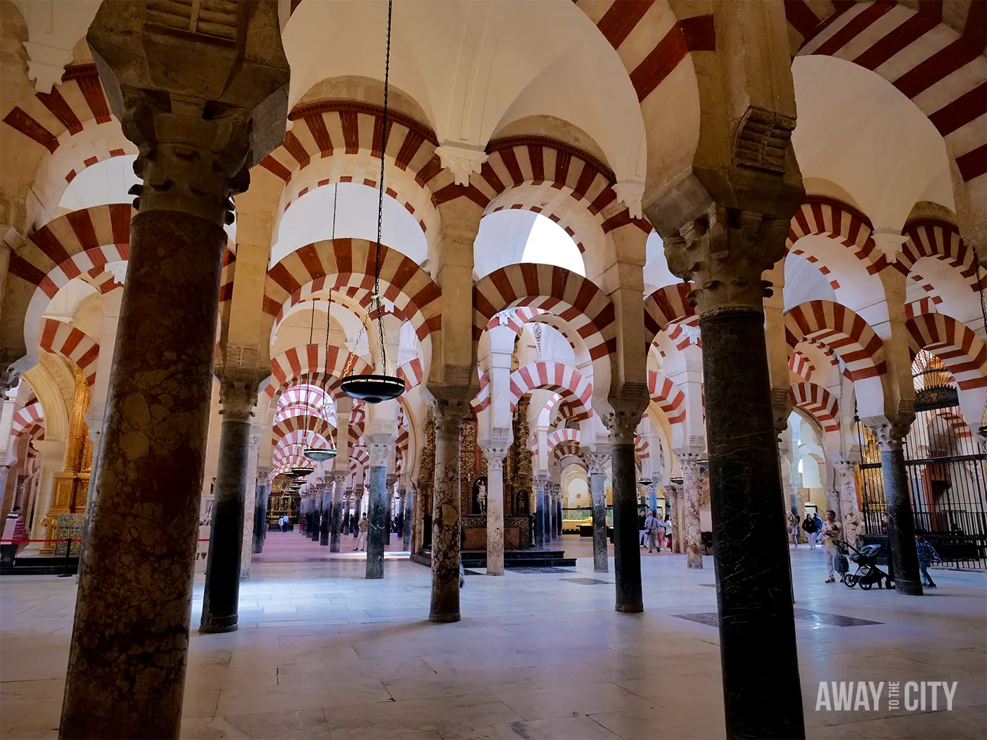 Interior of the Mezquita-Catedral in Cordoba, showing rows of red and white striped arches, stone columns, and a vast historic prayer hall.