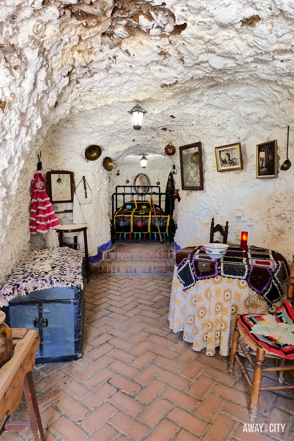 Interior of Museo Cuevas del Sacromonte in Granada, showing a traditional whitewashed cave dwelling with rustic furniture, ceramics, and arched ceiling.