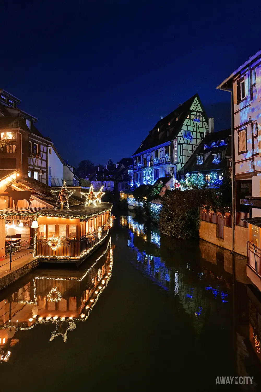 Canal in Colmar at night reflecting warm lights from surrounding buildings, with a calm waterway running through the historic town.