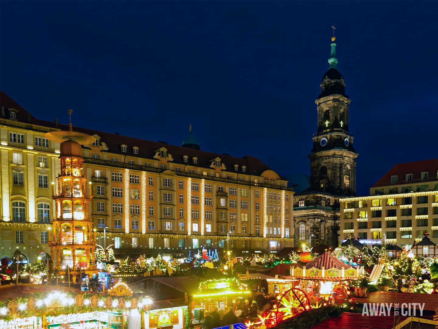 Illuminated square in Dresden at night with historic buildings, festive market lights, and a central tower rising above the scene.