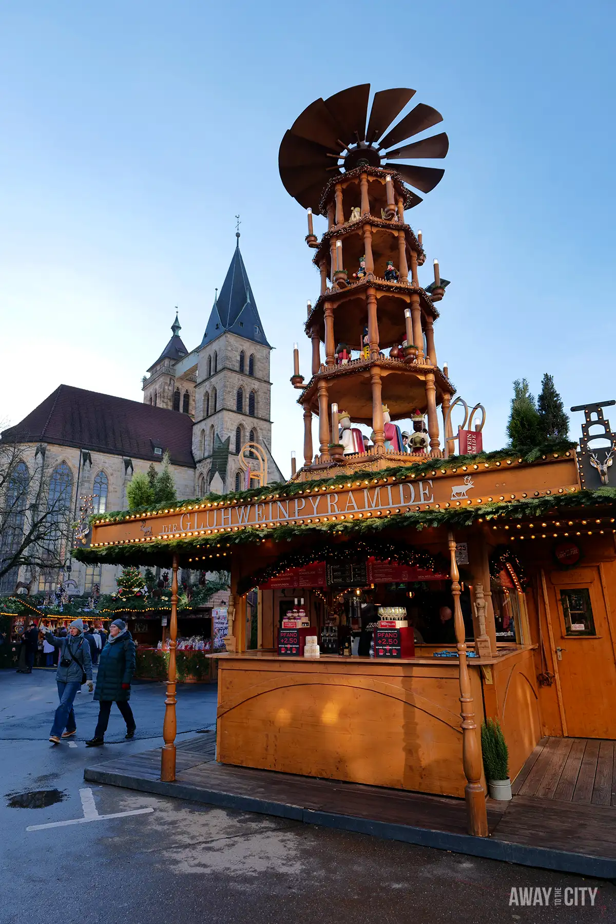 Wooden market stall in Esslingen with a tall decorative Christmas Pyramid, set against historic buildings and a cloudy sky.