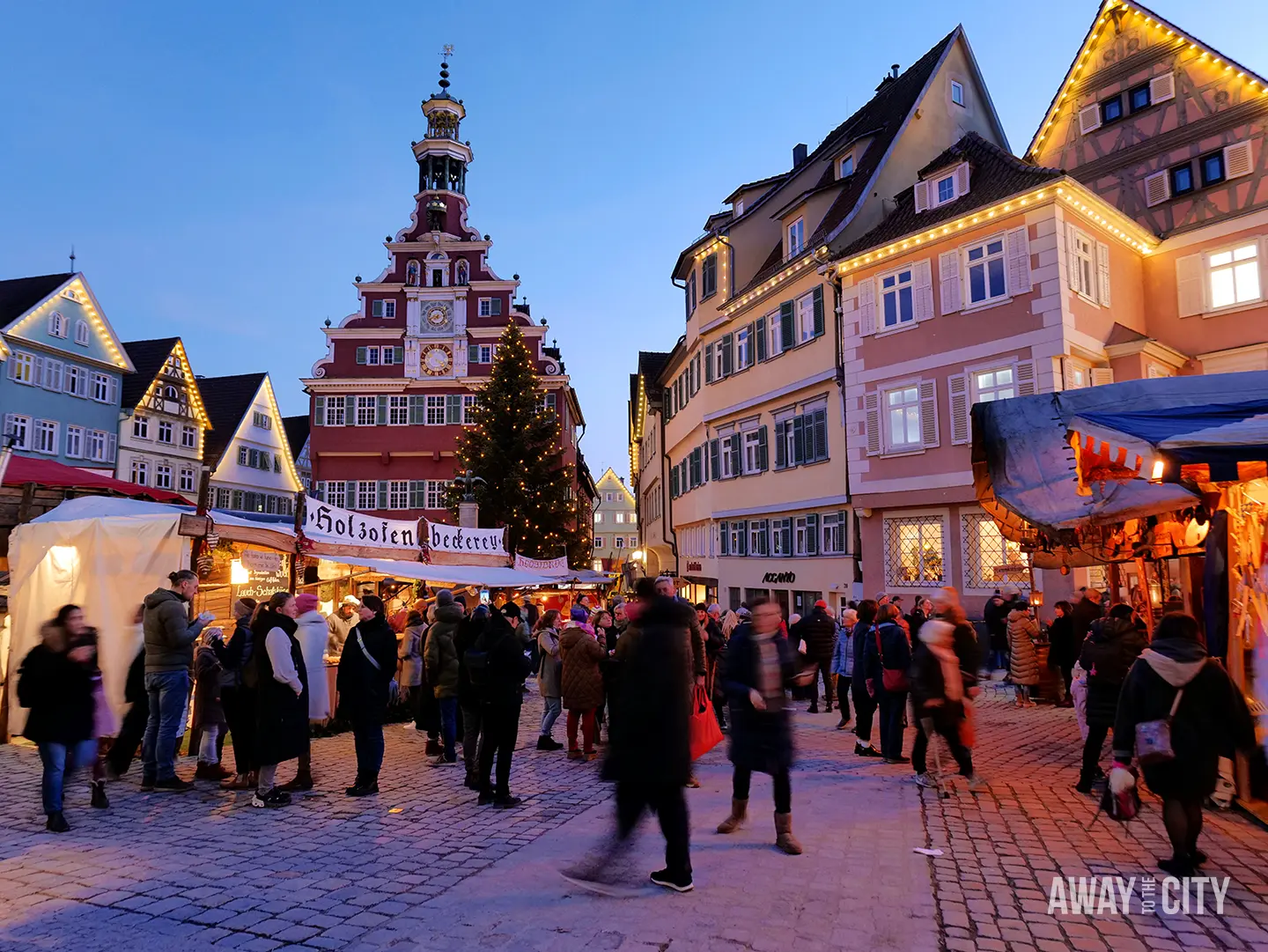 Festive street in Esslingen with colourful half-timbered houses, market stalls, and crowds walking through a warmly lit evening setting.