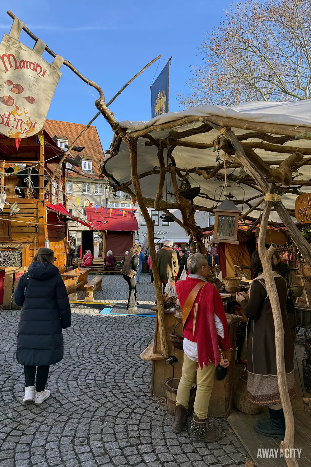 Medieval-style market stall in Esslingen with wooden structures and costumed people standing on a cobbled street during daytime.