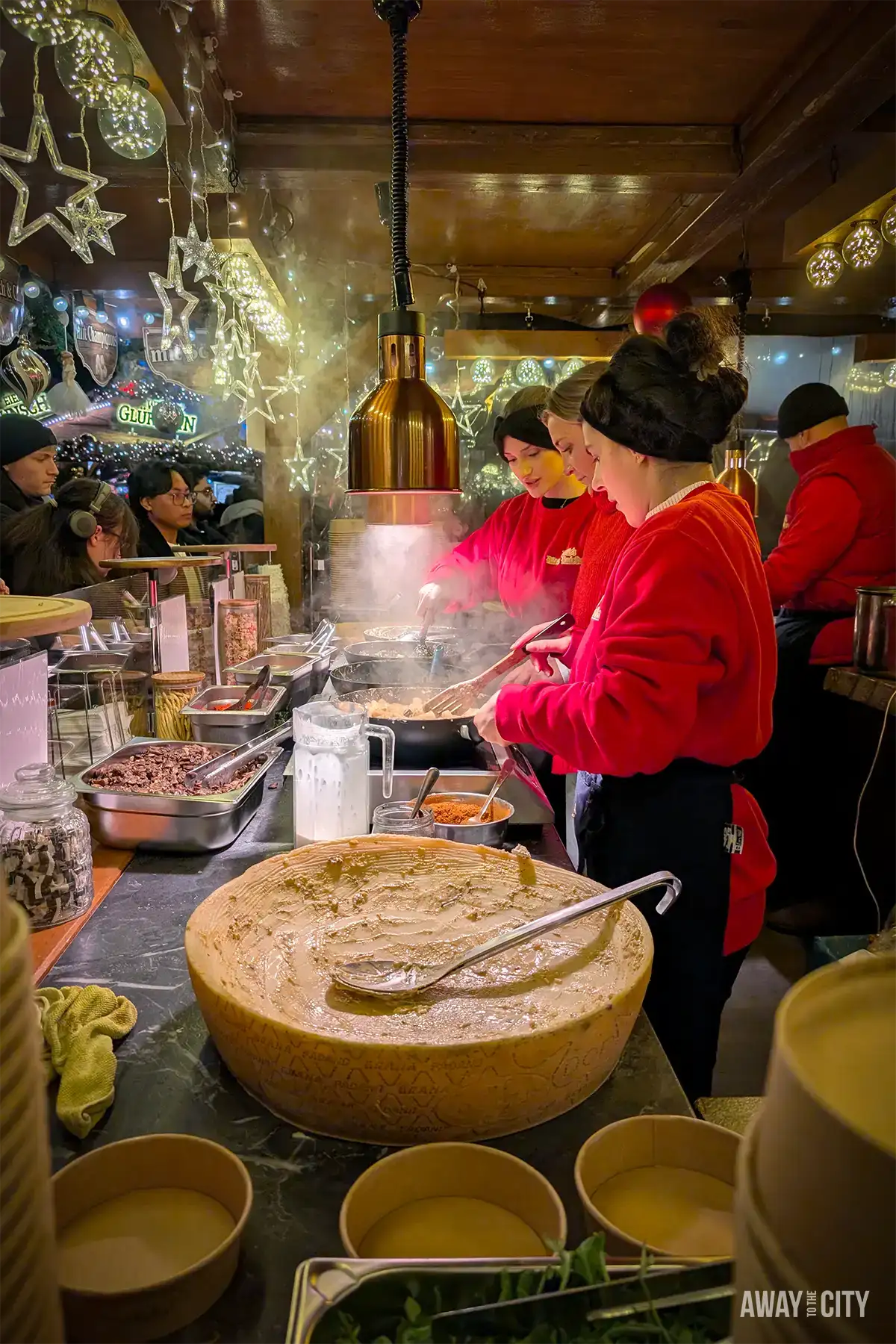 Market food stall in Nuremberg with a vendor in red serving hot dishes, large bowls and cooking pots visible on the counter.