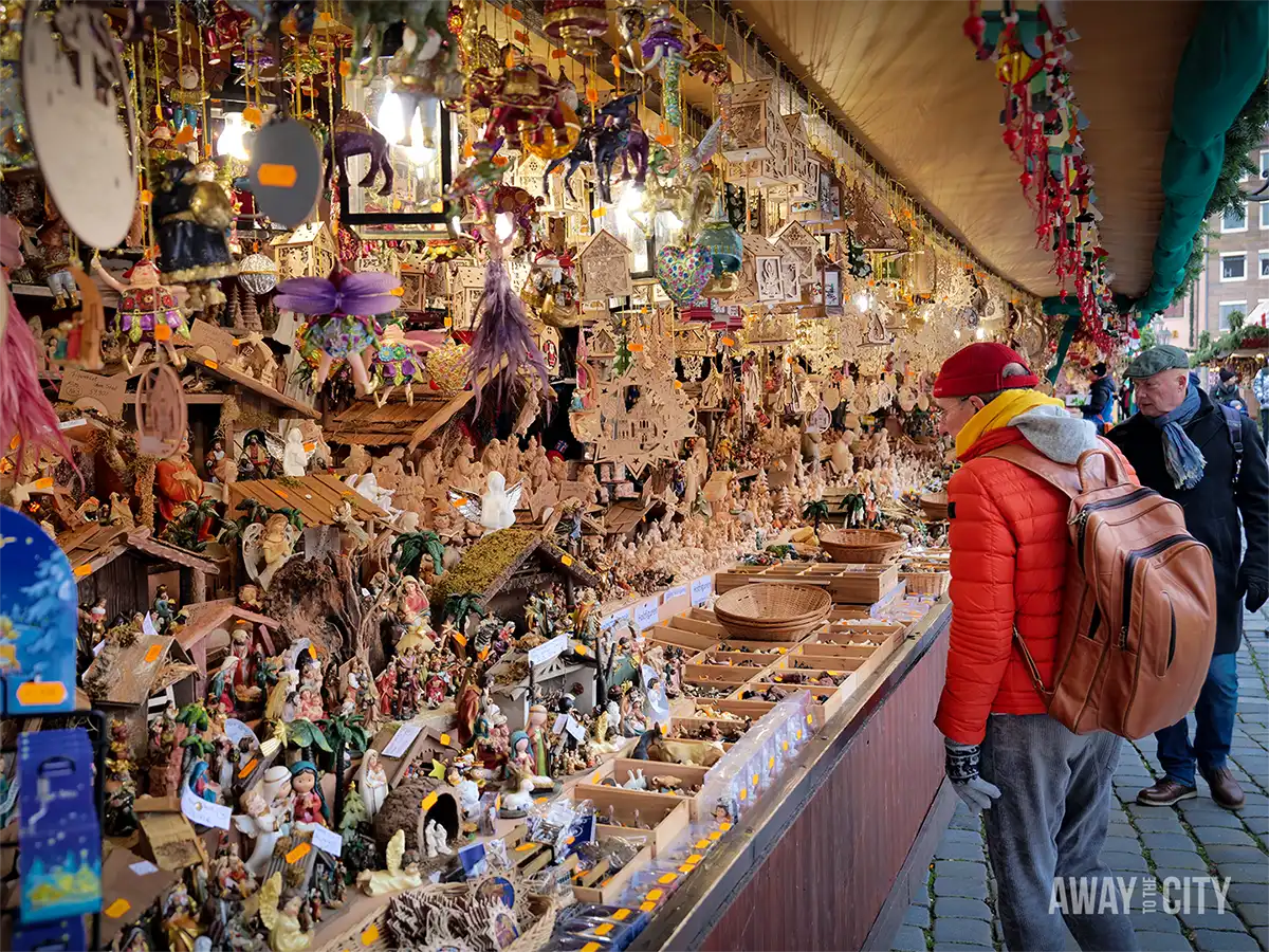 Crowded Nuremberg market stall filled with hanging ornaments and decorations, as a shopper browses under warm festive lighting.