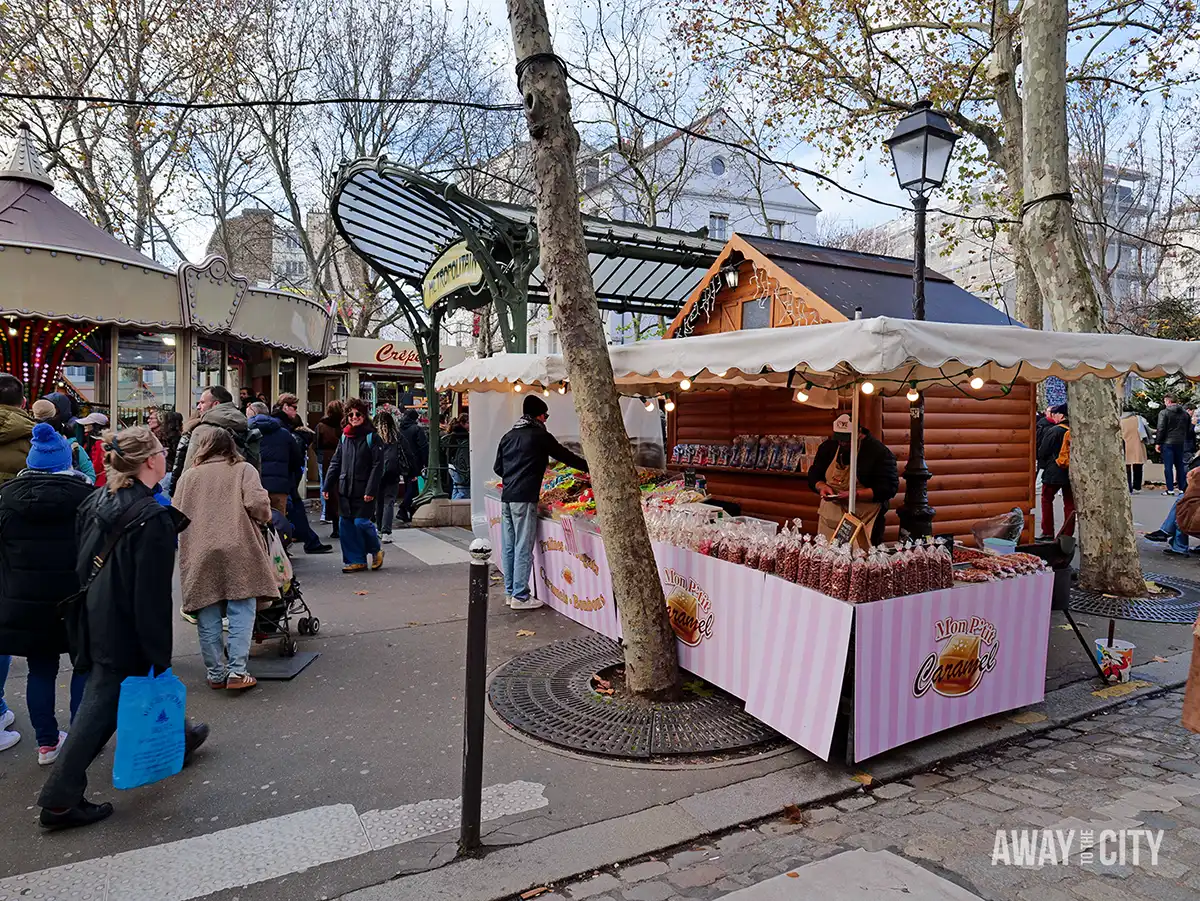Outdoor Christmas market in Paris with wooden stalls, bare trees, and people walking along a paved path during daytime.