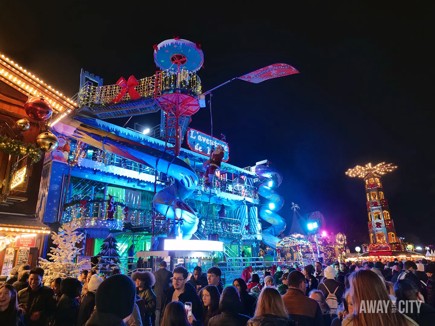 Nighttime fairground scene in Paris with bright neon rides, crowds of visitors, and colourful lights illuminating the lively atmosphere.