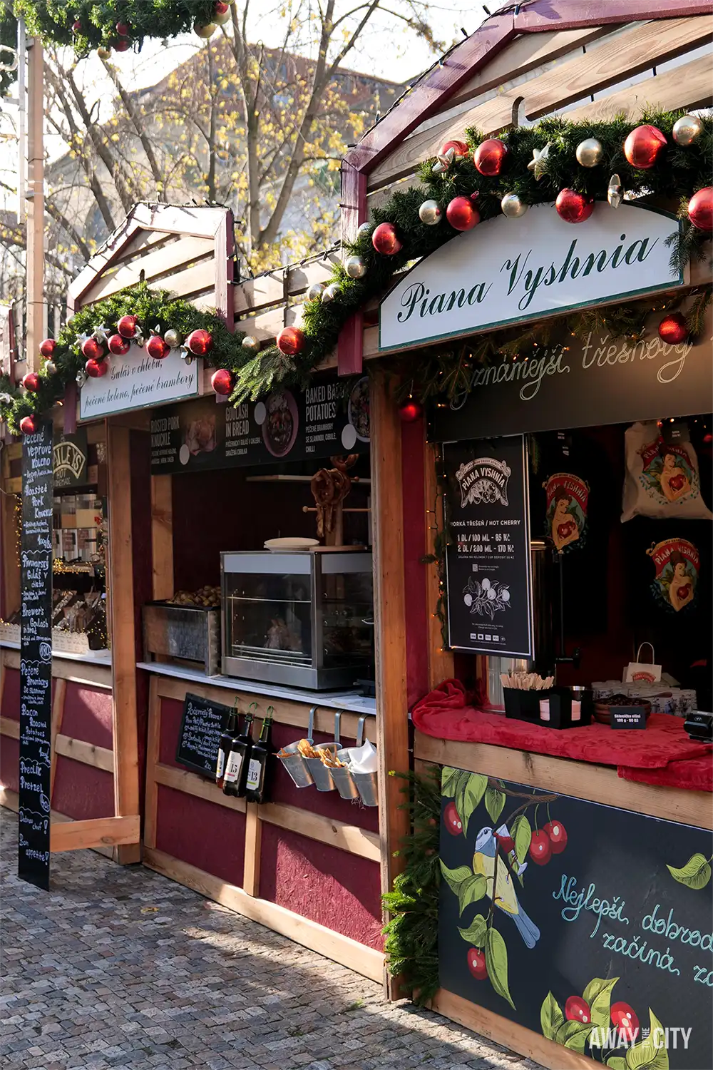 Traditional Prague market stall decorated with garlands and ornaments, displaying goods at a small wooden kiosk along a cobbled street.