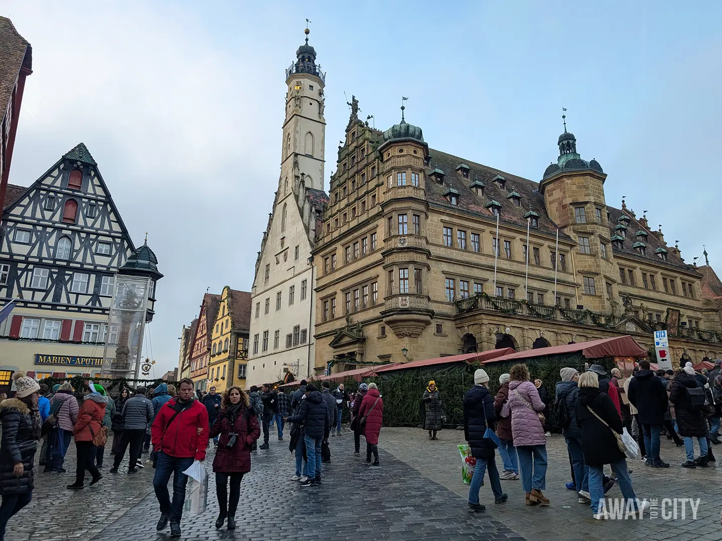 Busy square in Rothenburg with historic buildings and crowds walking across cobbled streets under a grey sky.