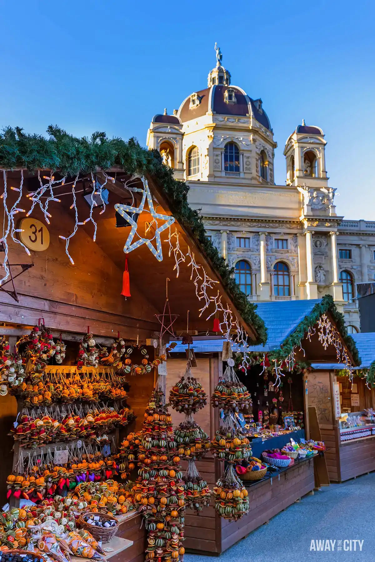 Vienna Christmas market stall displaying ornaments and gifts beside a historic church facade, with festive decorations and warm evening light.