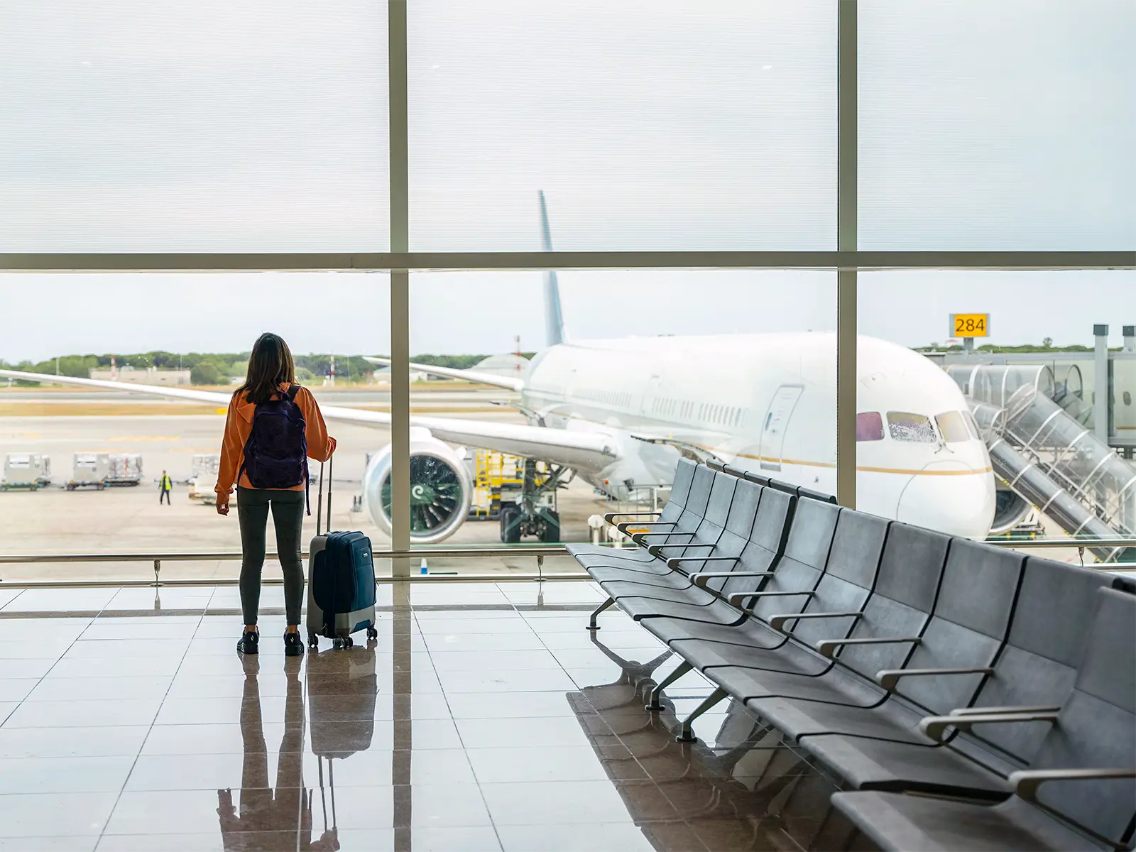 Traveller with a suitcase at an airport departure gate, symbolising a woman who knows hacks to find cheap flights.
