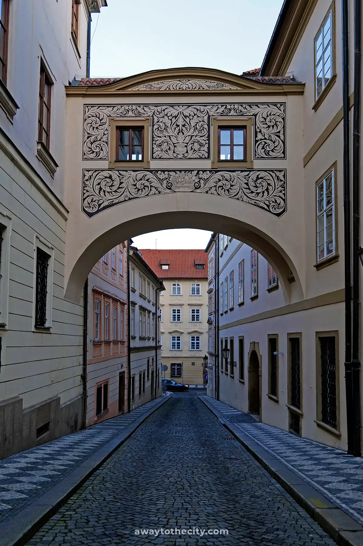 A cobble-stoned alleyway called Thunovska Street in Prague with an ornate bridge connecting two buildings above, one of the best hidden gems in the city.