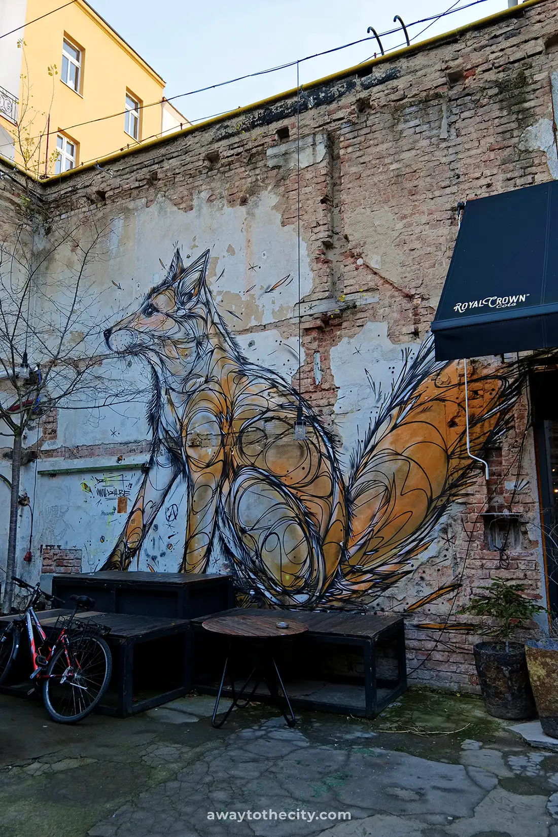 A vibrant mural of an orange fox on a weathered brick wall in a courtyard.