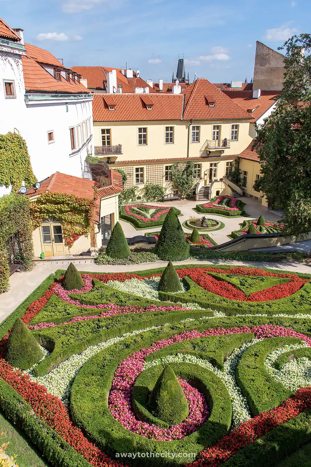 A manicured baroque garden in Prague, with swirling patterns of red, white, and pink flowers.