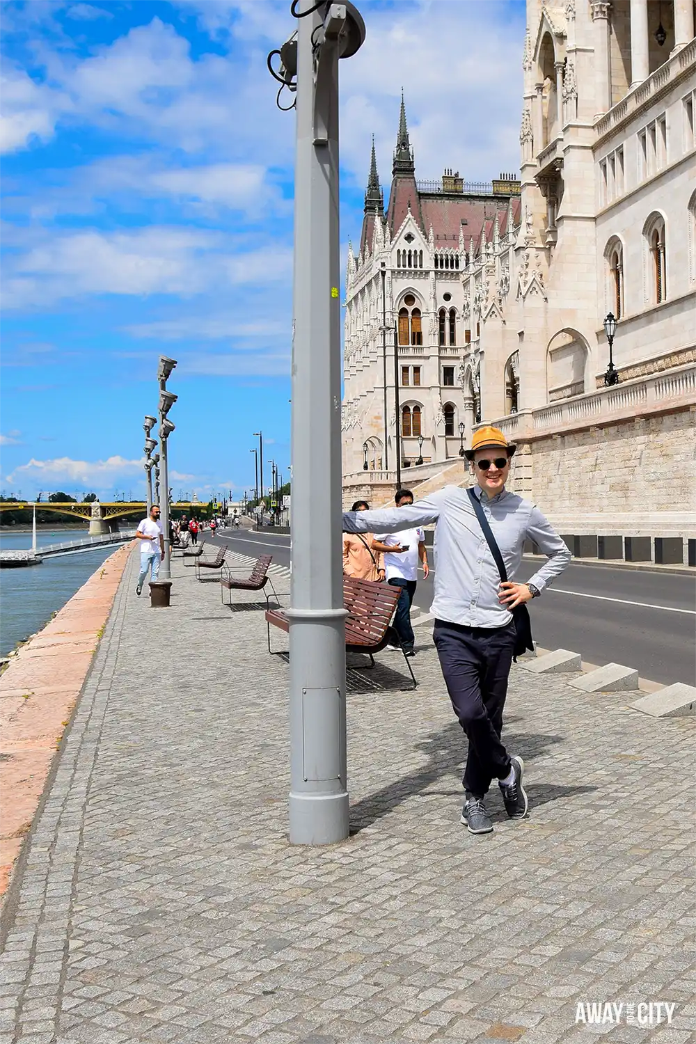Person leaning against a lamppost on the Danube Promenade in front of the Hungarian Parliament building.