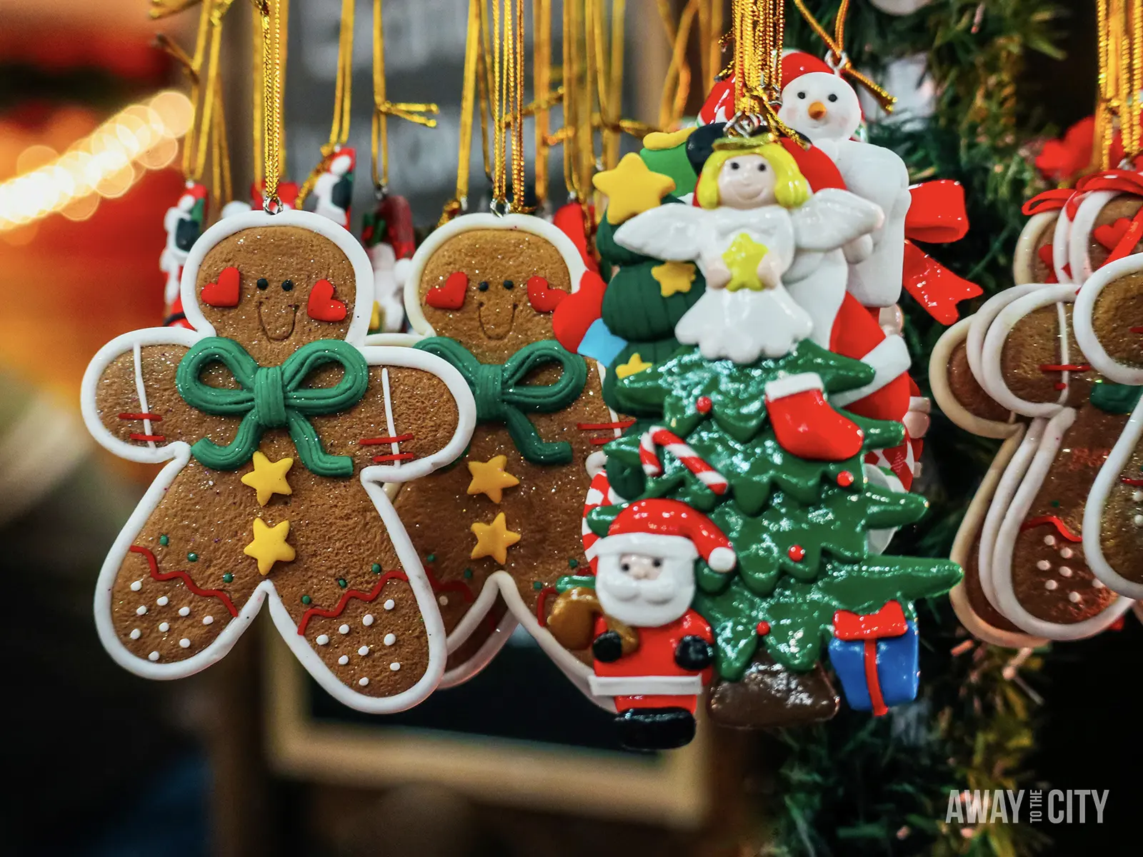 A close-up shot of Christmas tree ornaments for sale, featuring gingerbread men, a snowman, and Santa, hanging in a festive market setting.