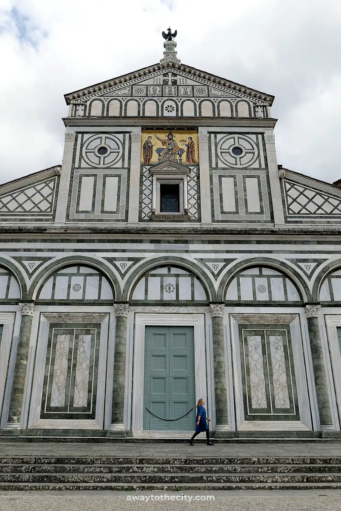 A person walks past the striking green and white marble facade of the Basilica di San Miniato al Monte.