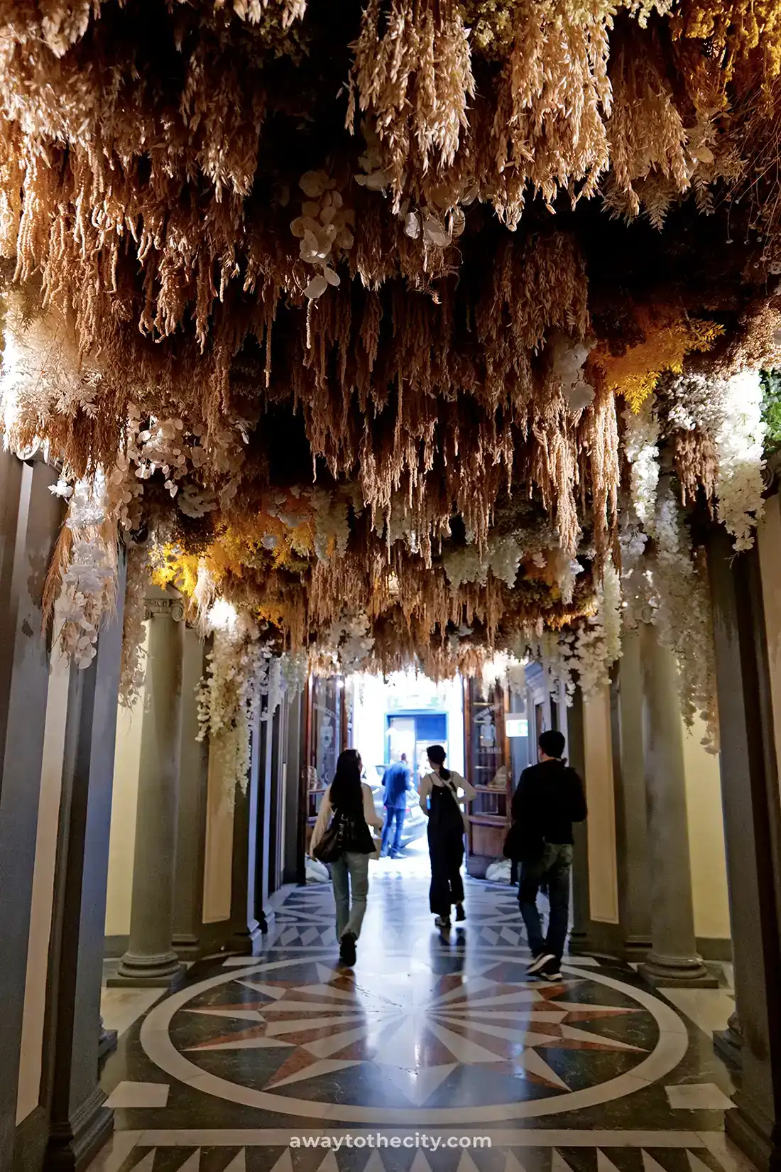 People stroll into the Officina Profumo-Farmaceutica di Santa Maria Novella beneath a striking floral installation.