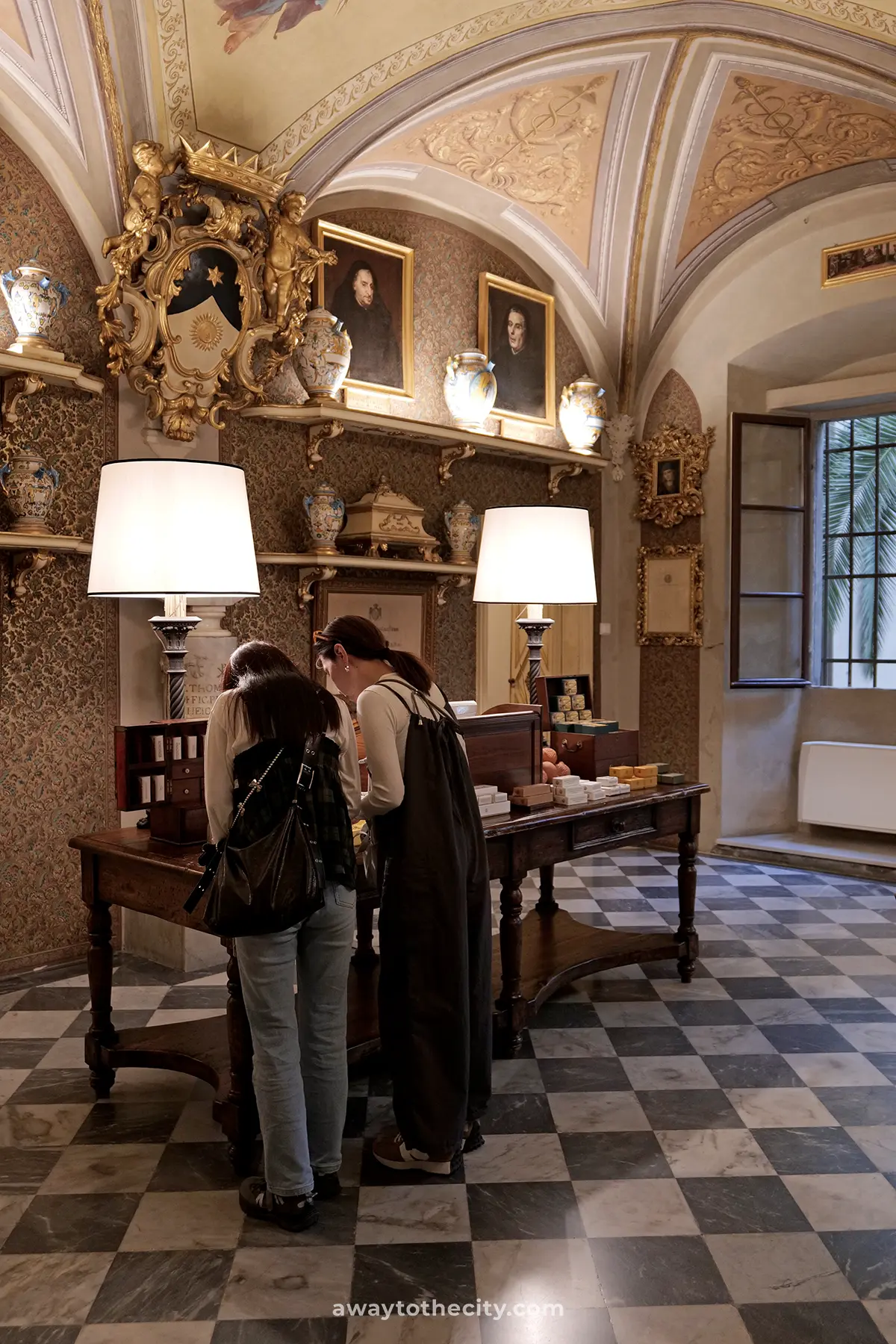 For the image of the vaulted ceilings: Two visitors examine products on a wooden table within the beautifully adorned Officina Profumo-Farmaceutica di Santa Maria Novella.